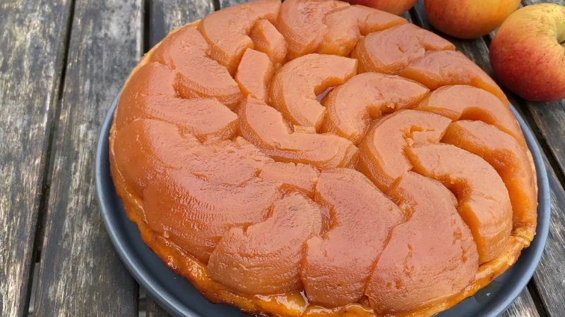 A Golden-Brown Tarte Tatin with Caramelized Apple Slices Arranged in A Circular Pattern on A Dark Plate