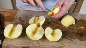 A Person Is Coring and Cutting Peeled Apples Into Quarters on A Wooden Cutting Board