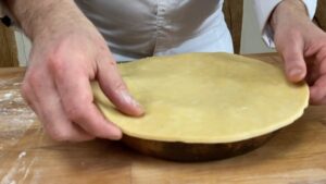 A Person in A White Chef's Coat Is Placing a Rolled-Out Pastry Sheet Over a Pan Filled with Apples for Tarte Tatin